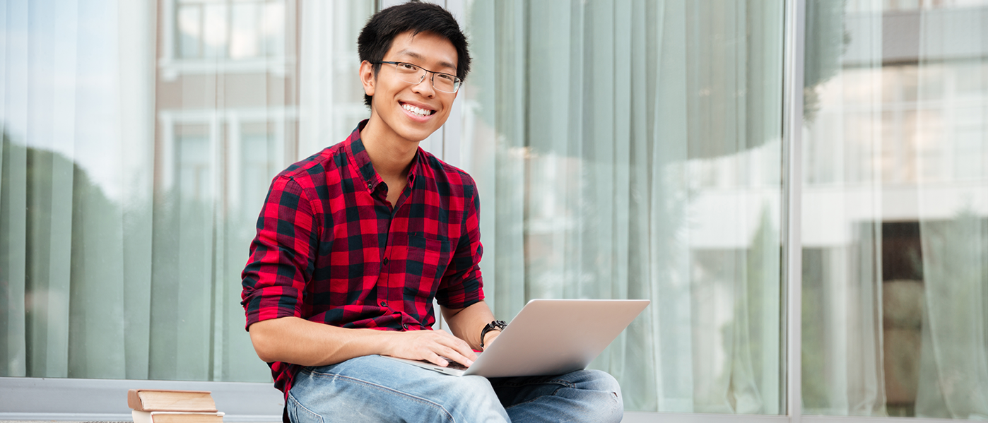 Happy young man in plaid shirt using laptop outdoors